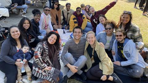 a picture of IP fellows smiling during the apple picking event, they are sitting on a picnic blanket together smiling